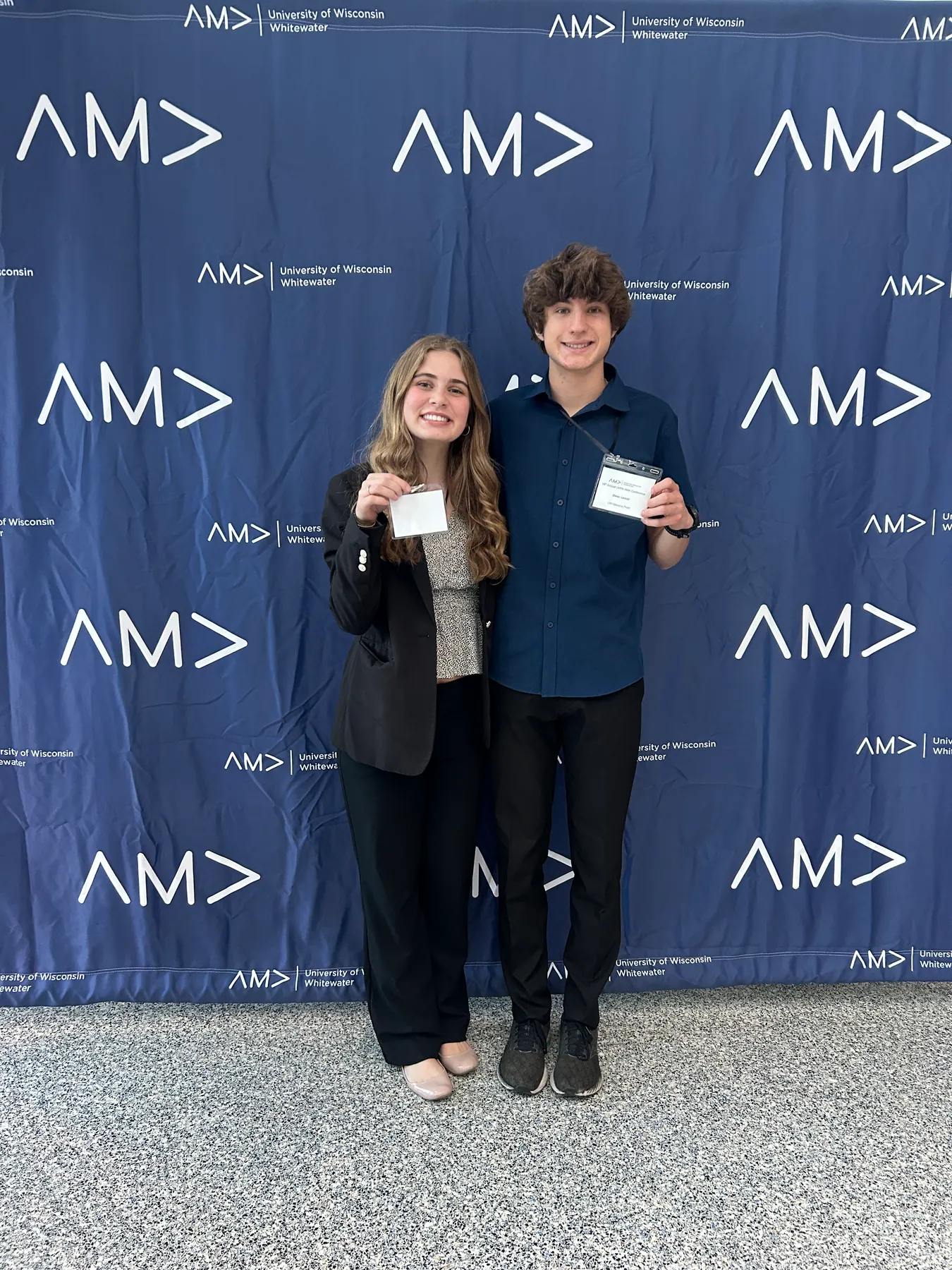 Two attendees holding their name badges in front of the AMA backdrop.