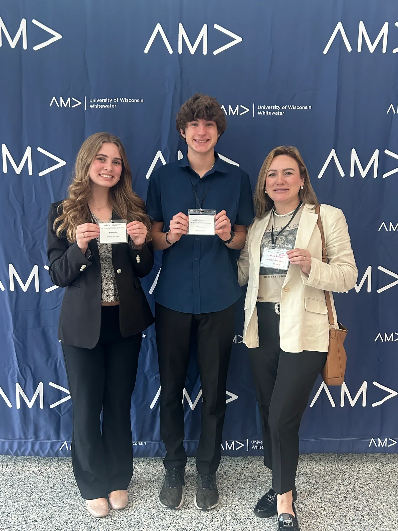 Three attendees standing together with name badges in front of the AMA backdrop.