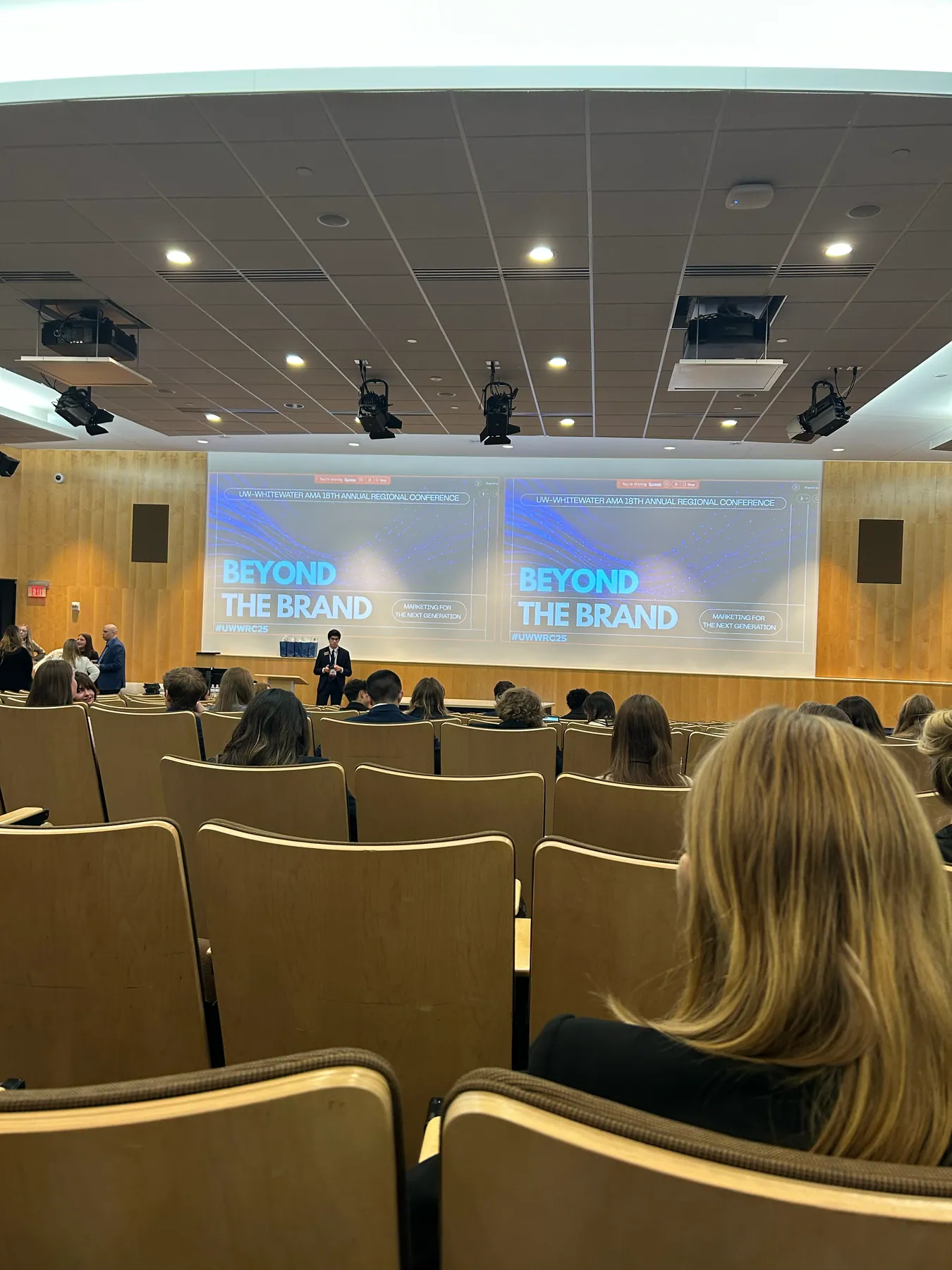Two projection screens reading Beyond the Brand above the audience at the UW–Whitewater AMA 18th annual regional conference.